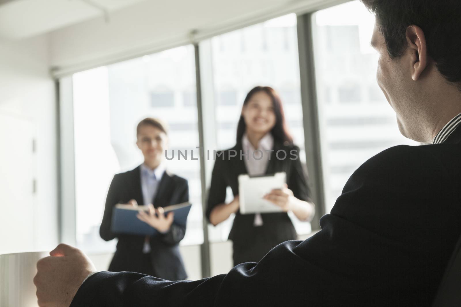 Two businesswomen standing up and presenting during a business meeting as a businessman watches by XiXinXing