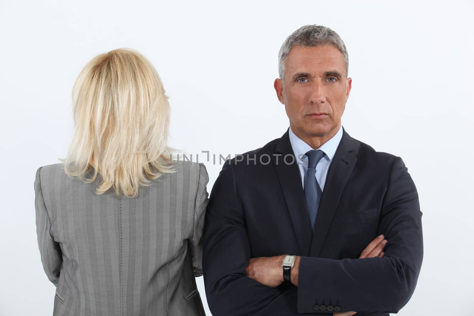 handsome businessman cross-armed and female businesspartner with back turned to camera by phovoir