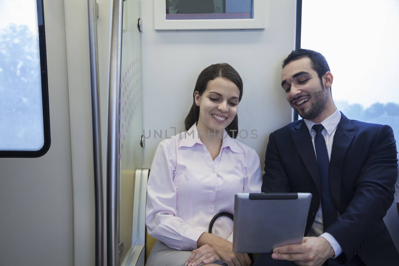 Two young business people sitting and looking at a digital tablet on the subway