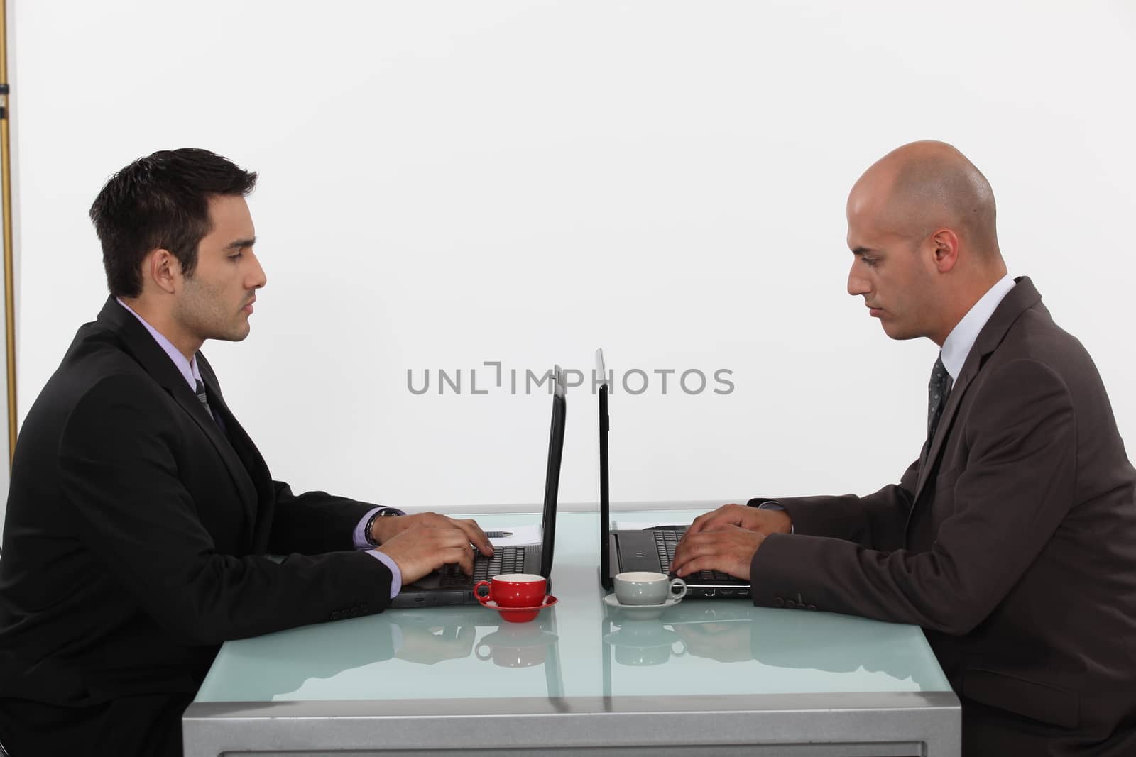 Two businessmen with coffee and laptops by phovoir