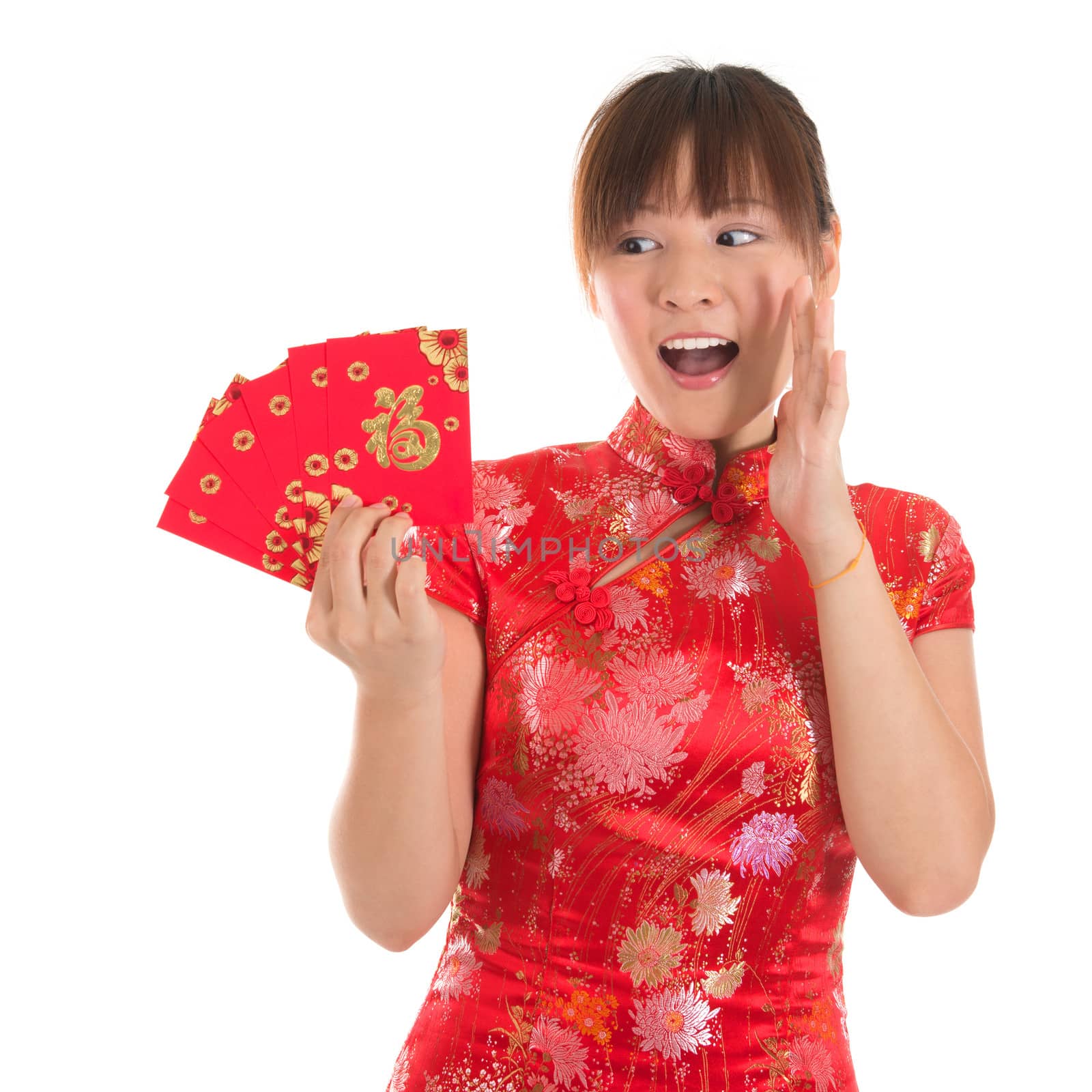 Asian woman with Chinese traditional dress cheongsam or qipao holding ang pow or red packet monetary gift showing surprise face expression. Chinese new year concept, female model isolated on white background.