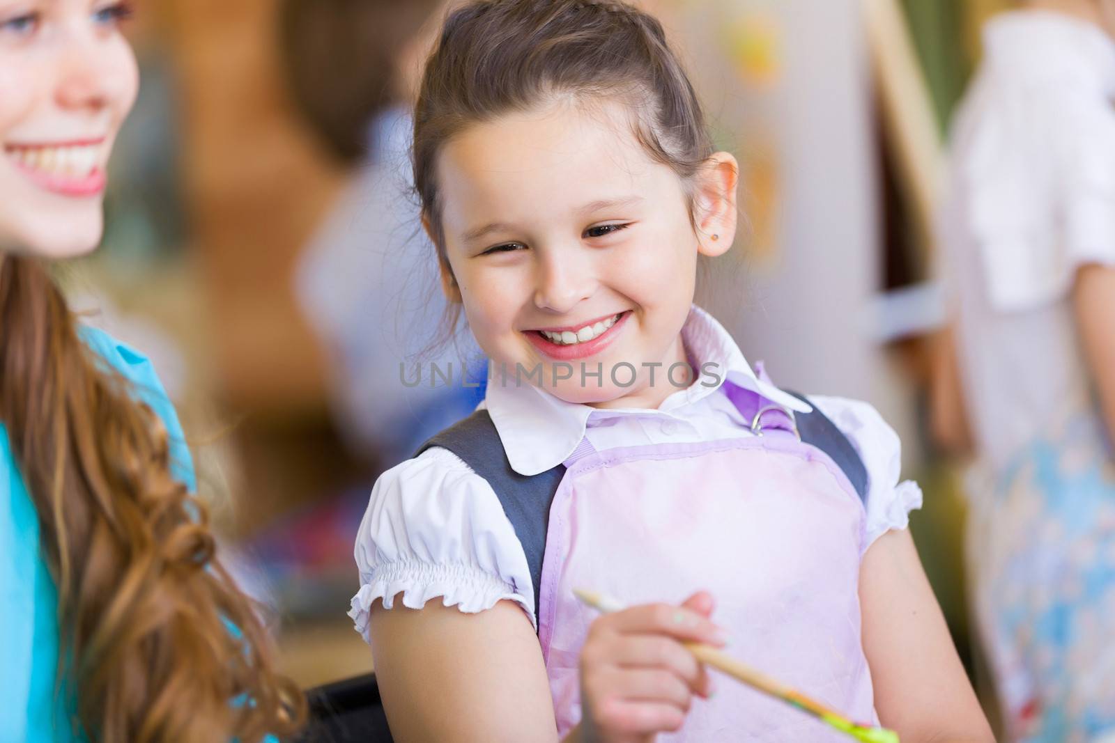 Little girl painting with teacher at kindergarten