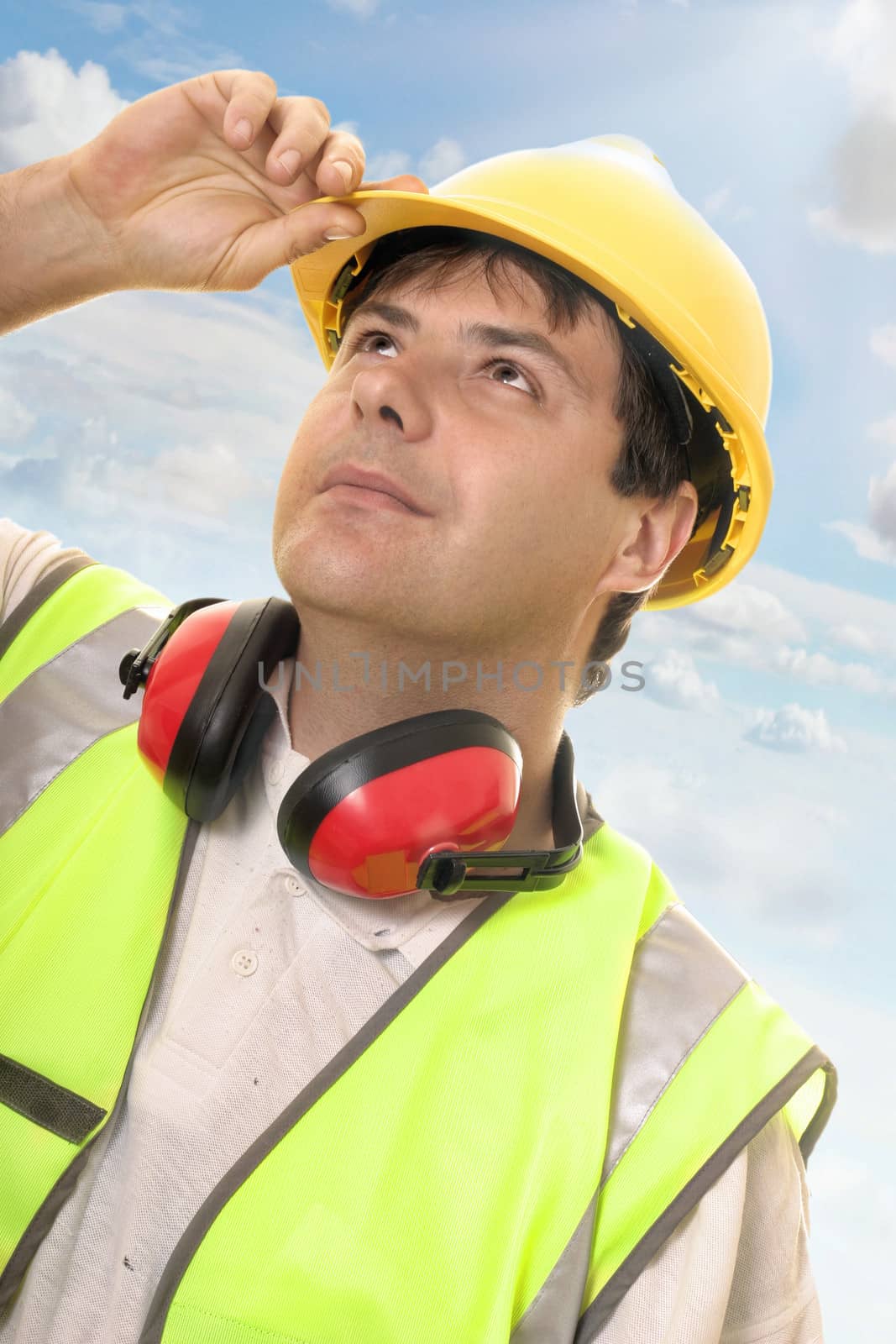 Hard working builder, construction worker or foreman looking up or overseeing progress.  Sunlit sky and clouds background

