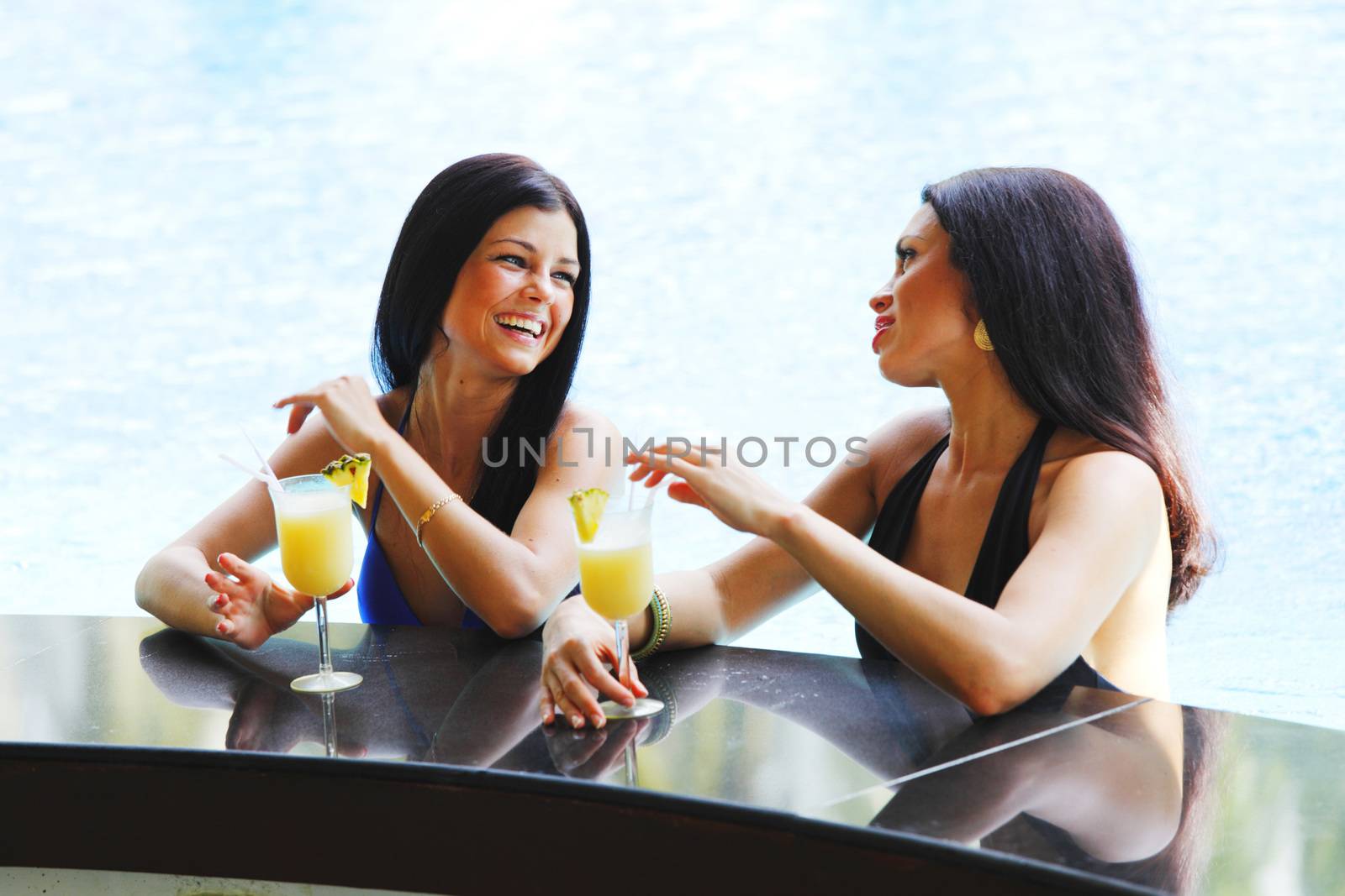 Two women with cocktails in swimming pool by Yellowj