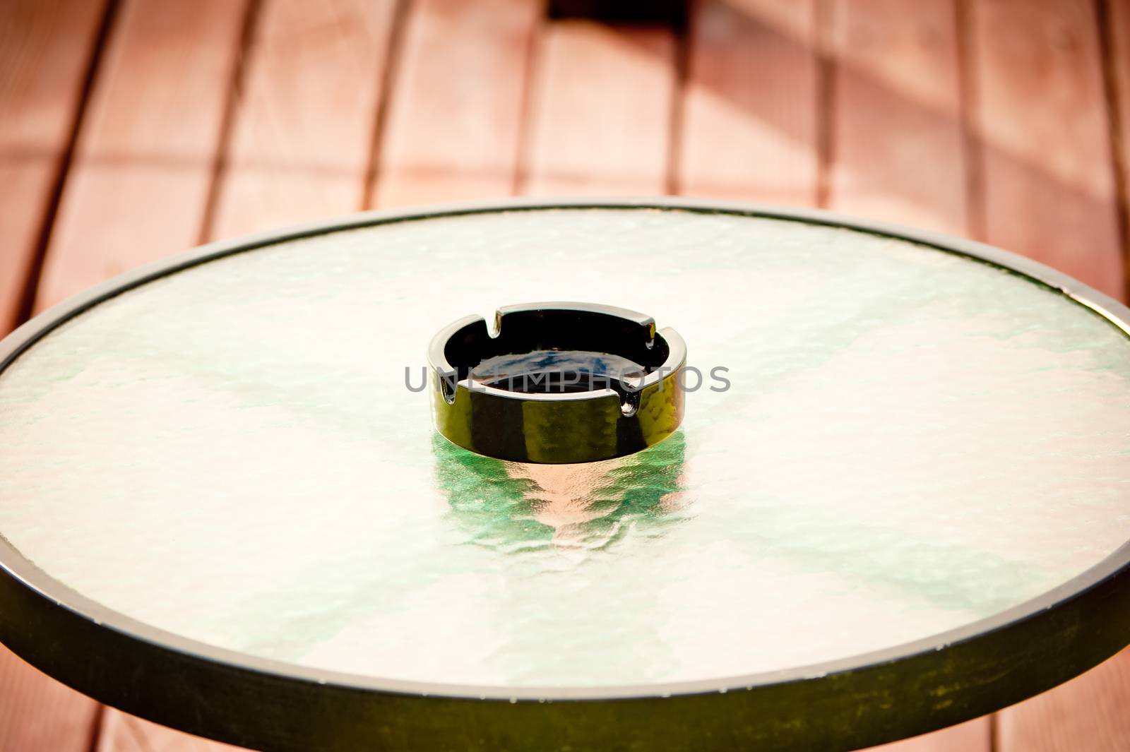 black empty ashtray stands in the middle of a round glass table by kosmsos111