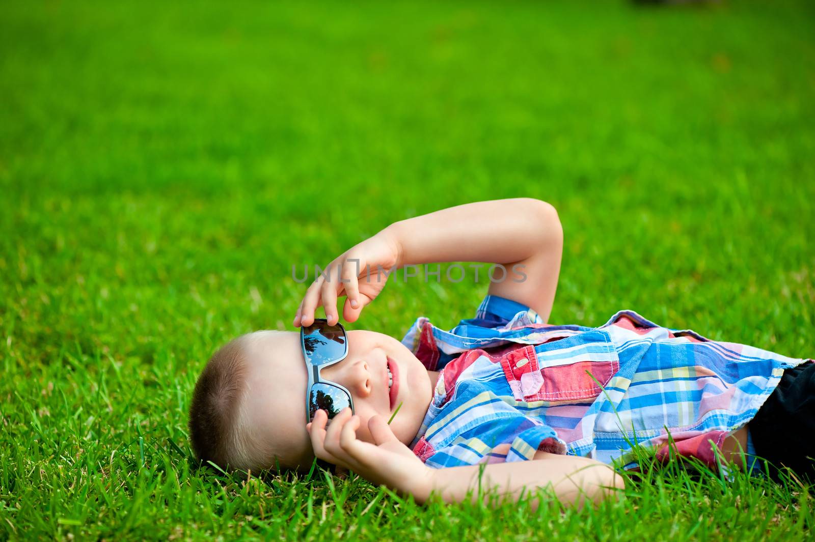 happy boy resting lying on green grass in sunglasses by kosmsos111