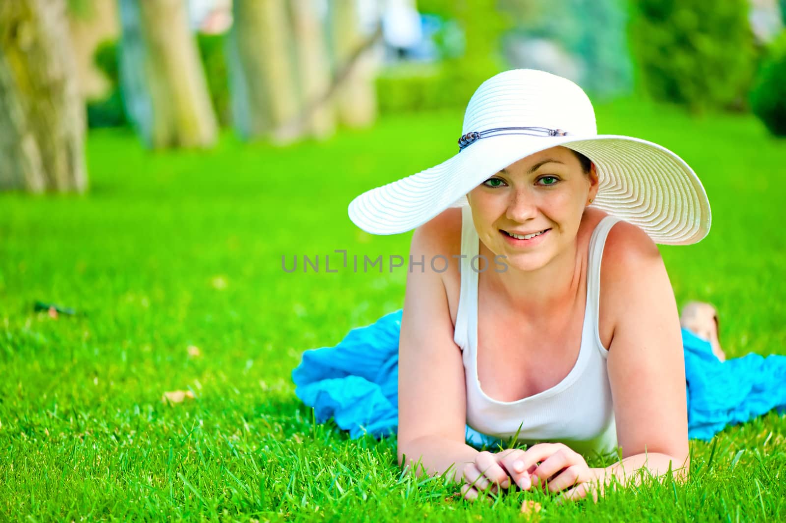 young beautiful smiling girl relaxing on the lawn in a white hat