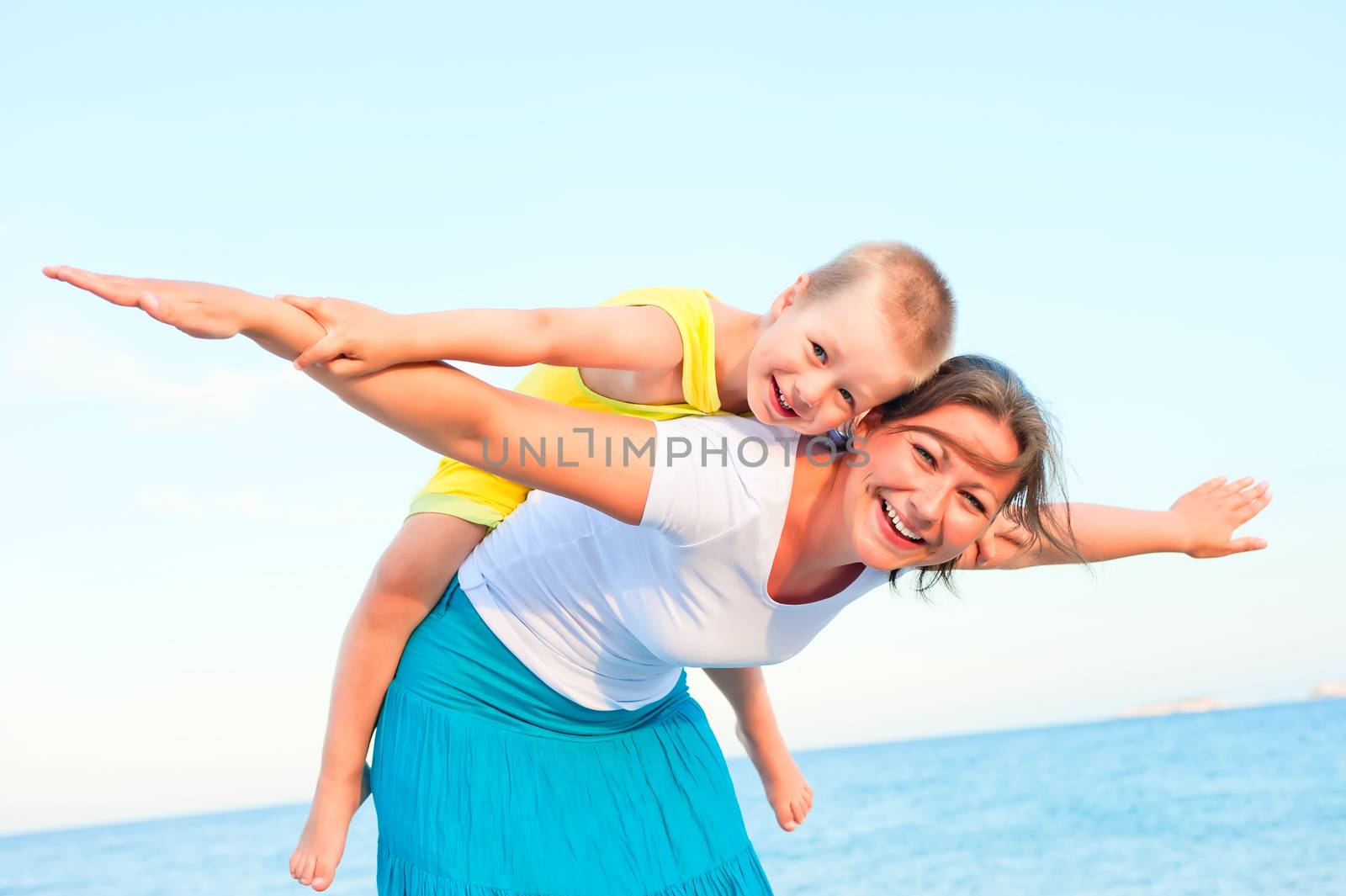 mother and son sitting on her back, happy playing on the beach