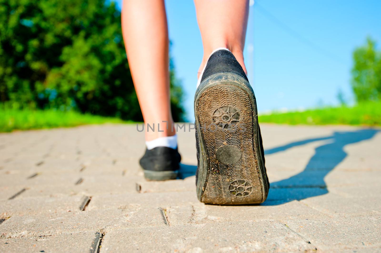 female legs in sneakers close up running down the road in the morning