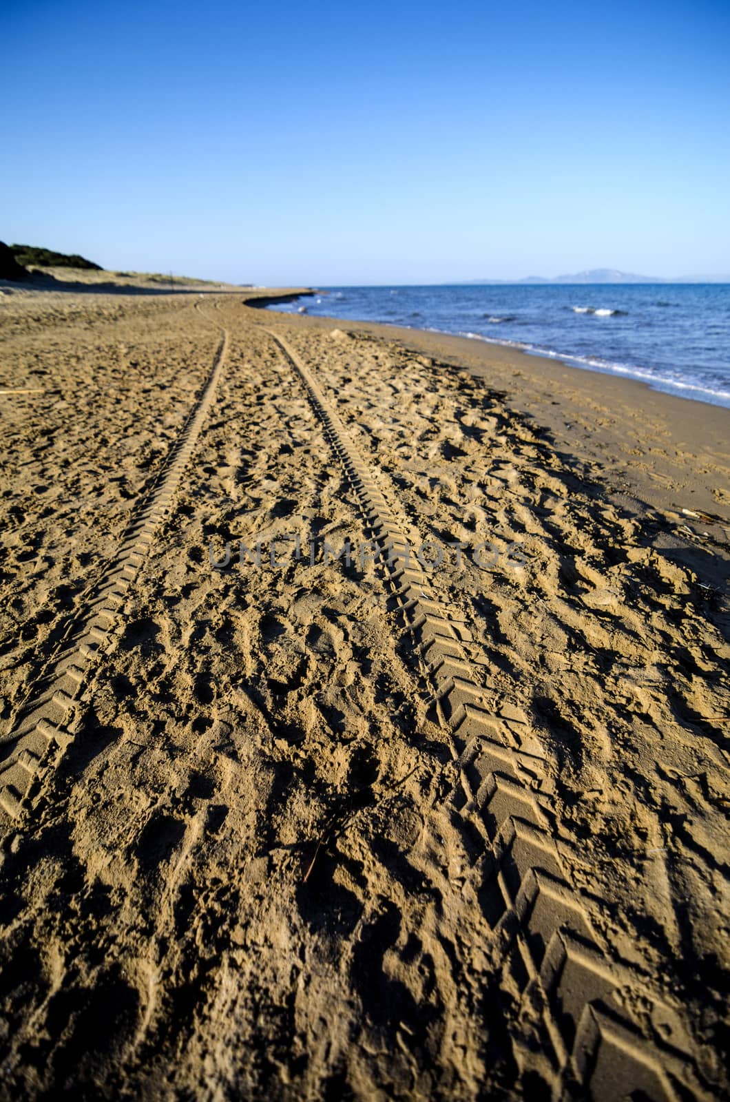 Quad bike tyre tracks on a sandy beach in Greece.