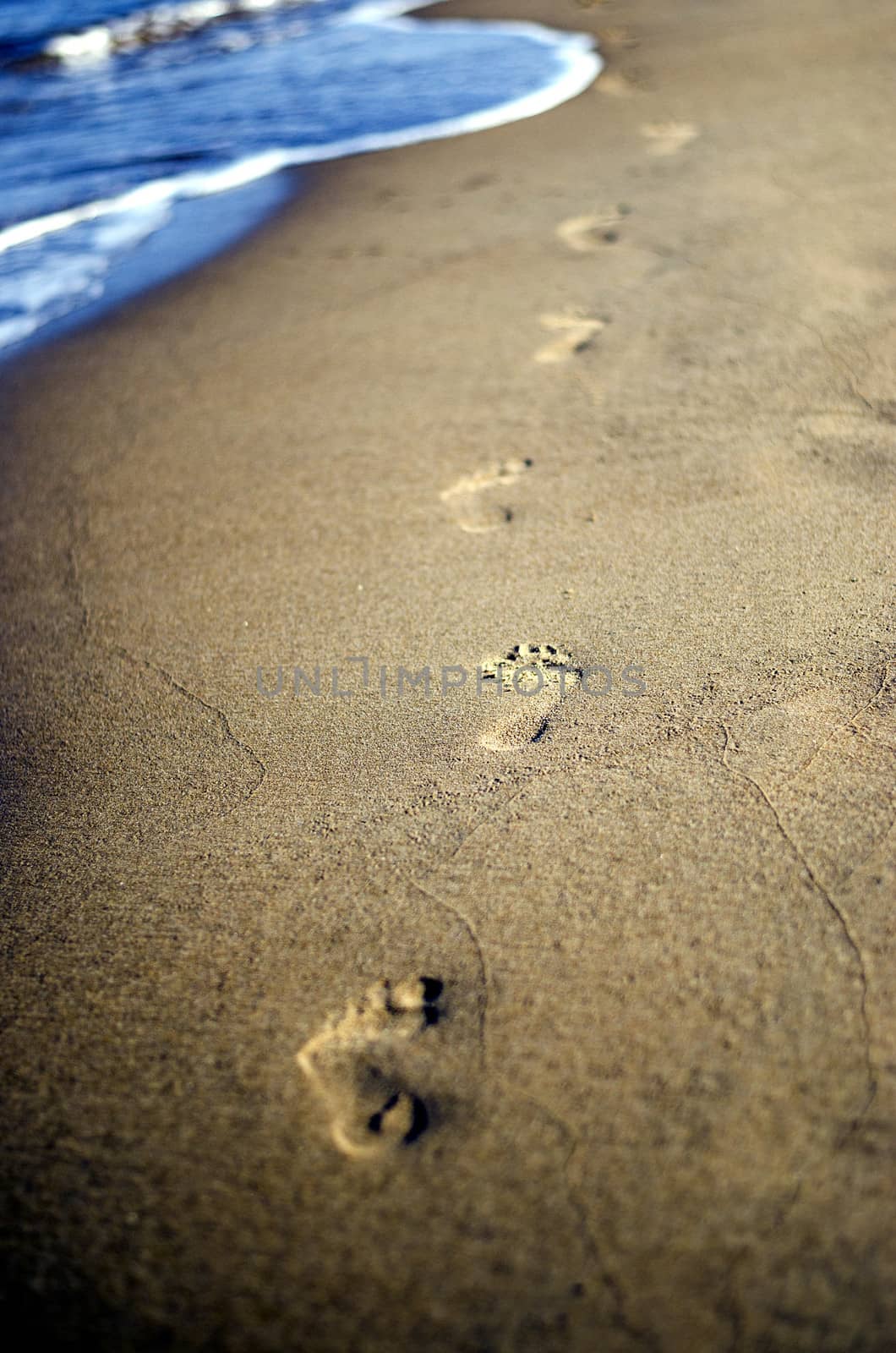 Barefoot footsteps in a sand with sea waves in background.