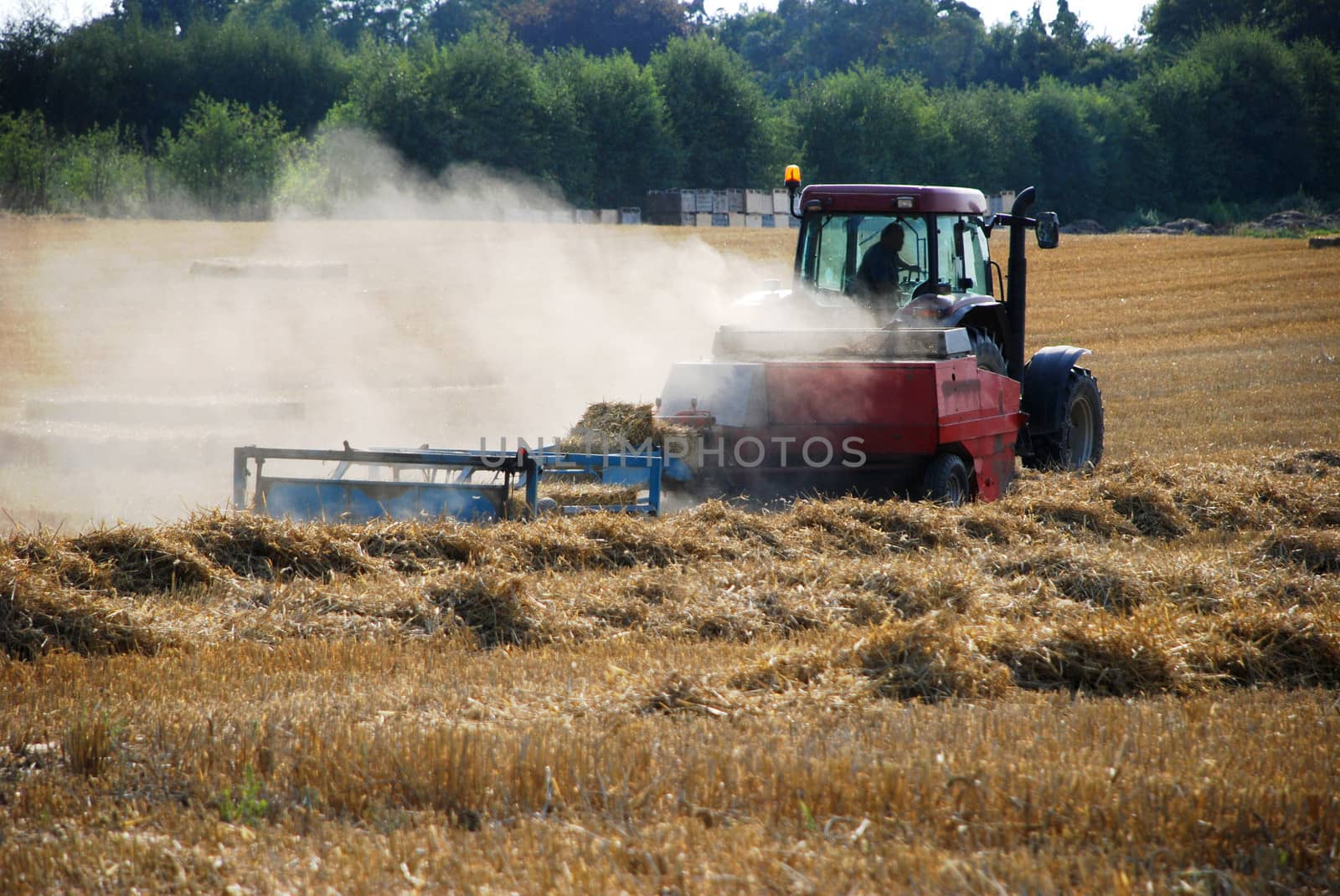 Red tractor baling straw in the countryside