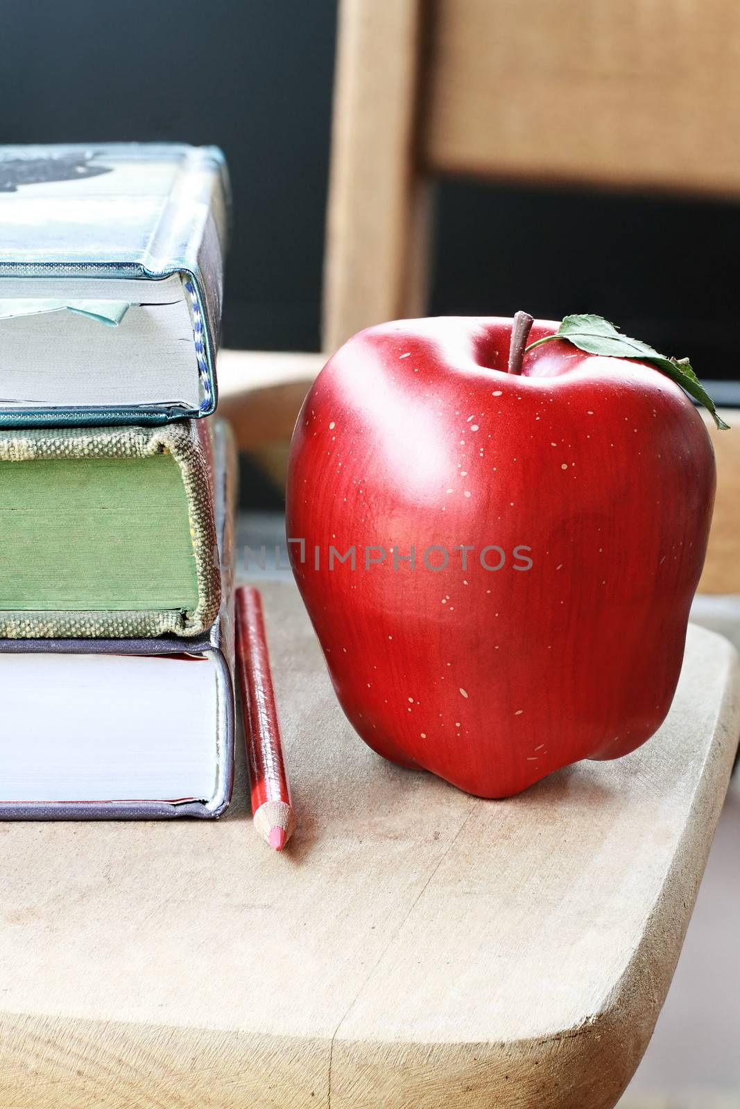 School books with apple and red pencil on desk. 
