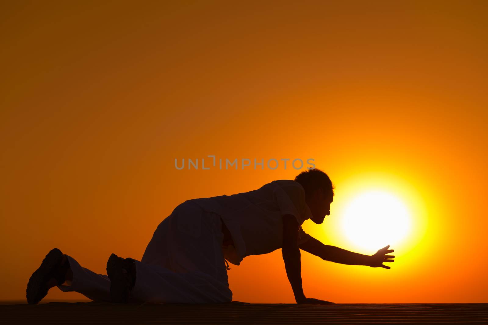 Tired and weaken man on all fours reached his hand to gold sunset sun disk to pray for help