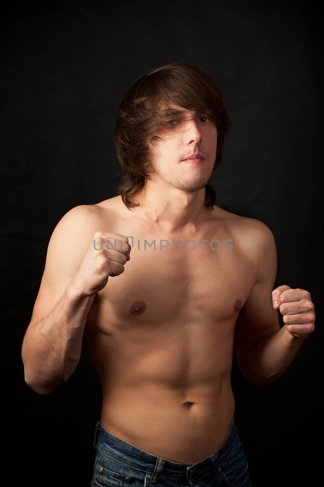 Athletic shirtless male in a strong pose on a black background