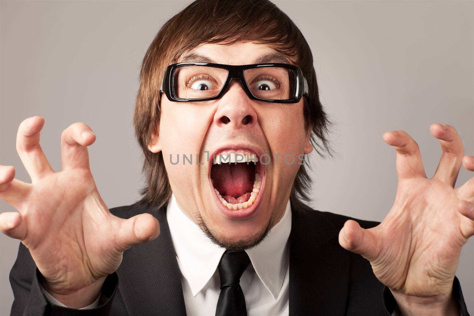 Stilish businessman screaming ang expressing anger. On a grey background