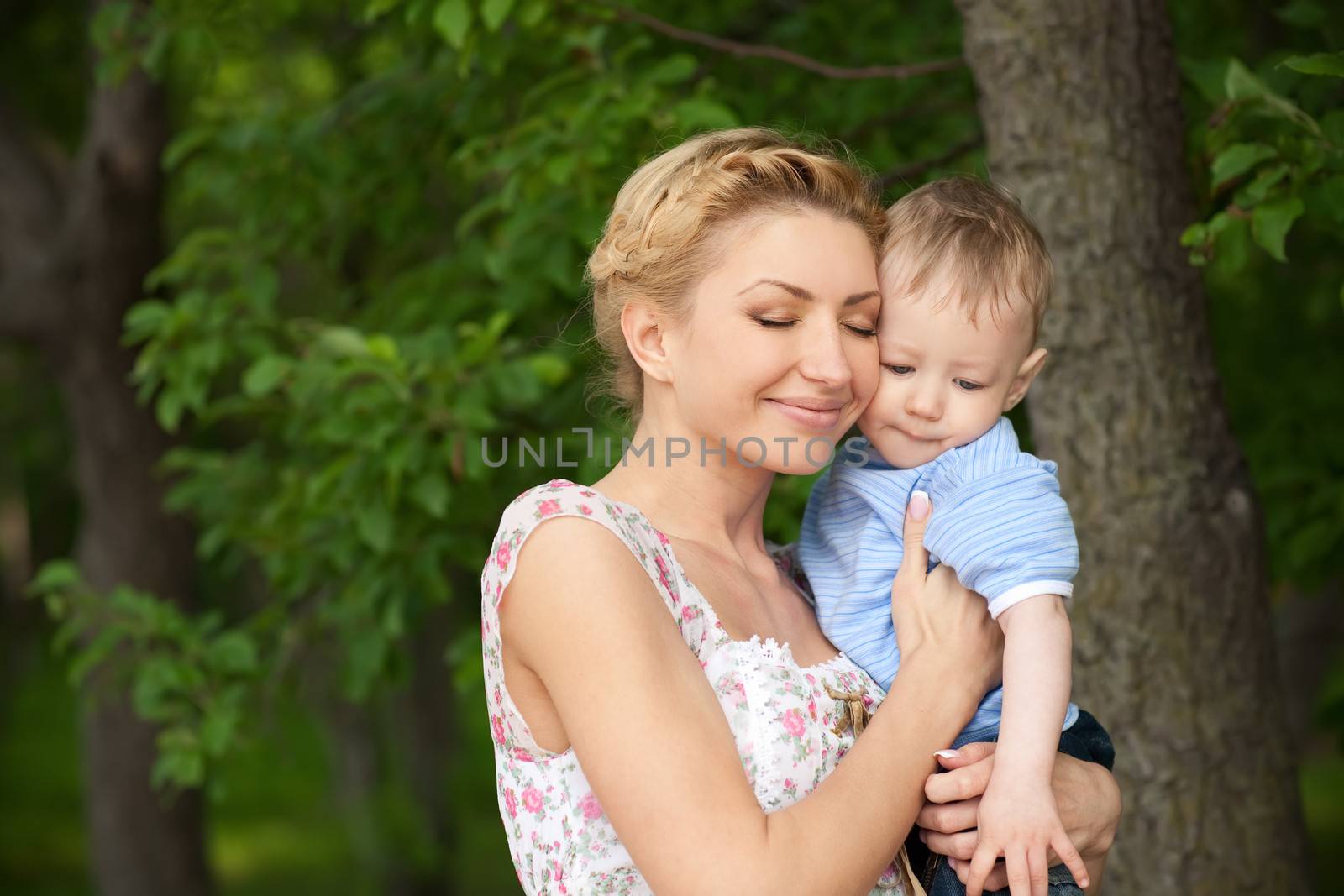 happy blond mom with her little son enjoying nature on a background of green leaves. Much of copyspace