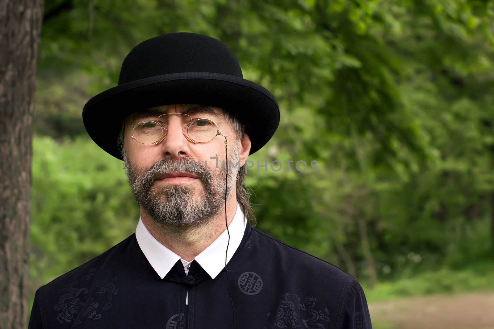 Portrait of a senior businessman, wearing a suit and hat, as well as old fashion eyeglasses. Outdoors.