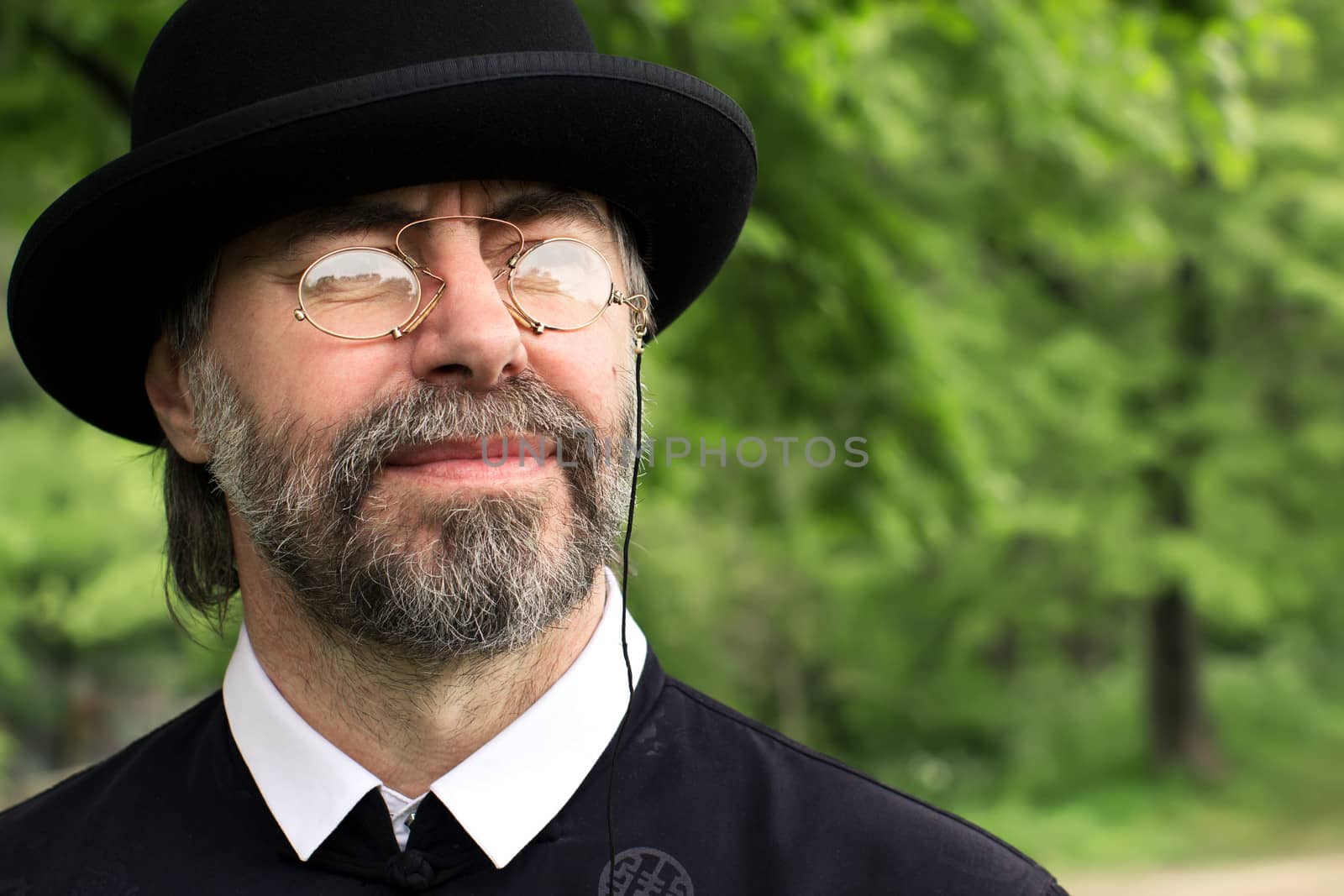 Portrait of a senior businessman, wearing a suit and hat, as well as old fashion eyeglasses. Outdoors.