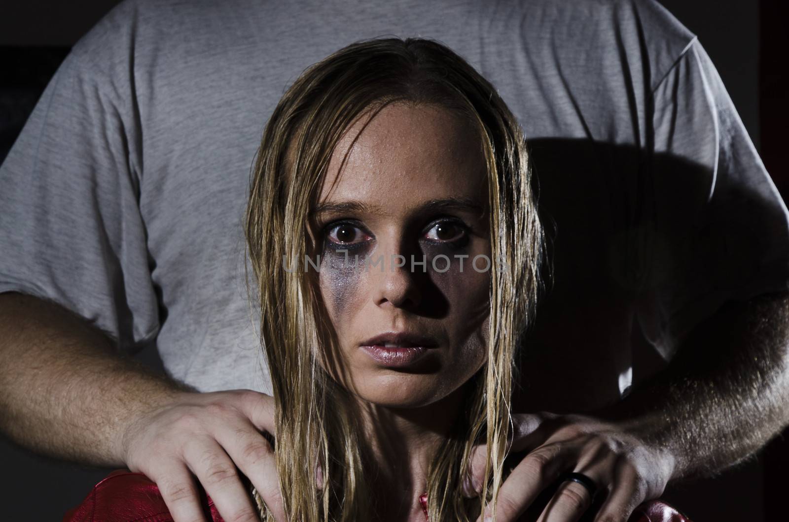 portrait of an abused woman with untidy hair and smudged makeup with a man standing behind her holding his hands on her shoulders cropped horizontally