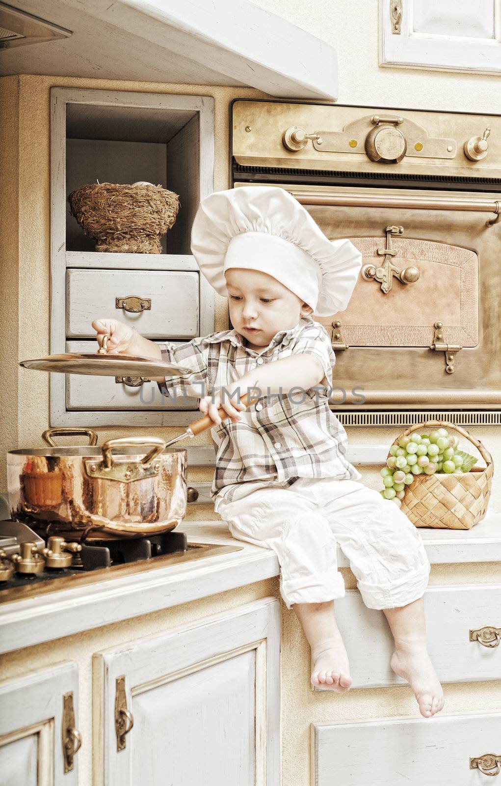 little boy sits on a kitchen table and plays the cook