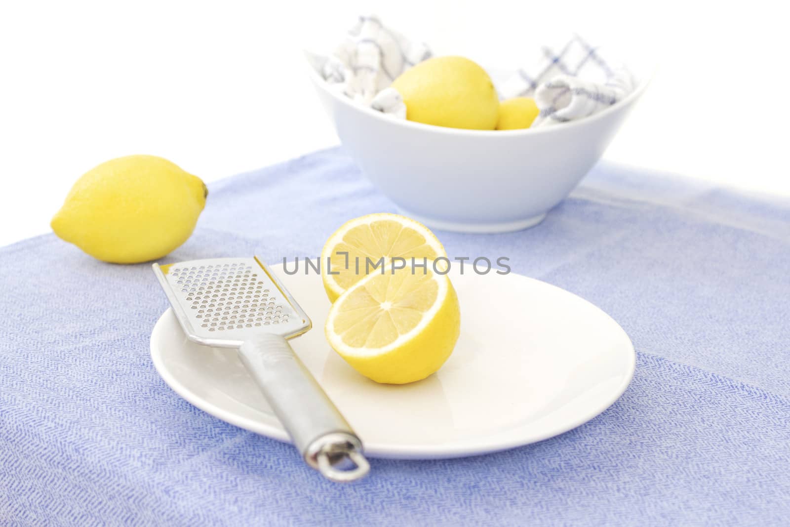 Unwaxed lemons on a plate with a lemon zester, and a bowl of lemons in the background