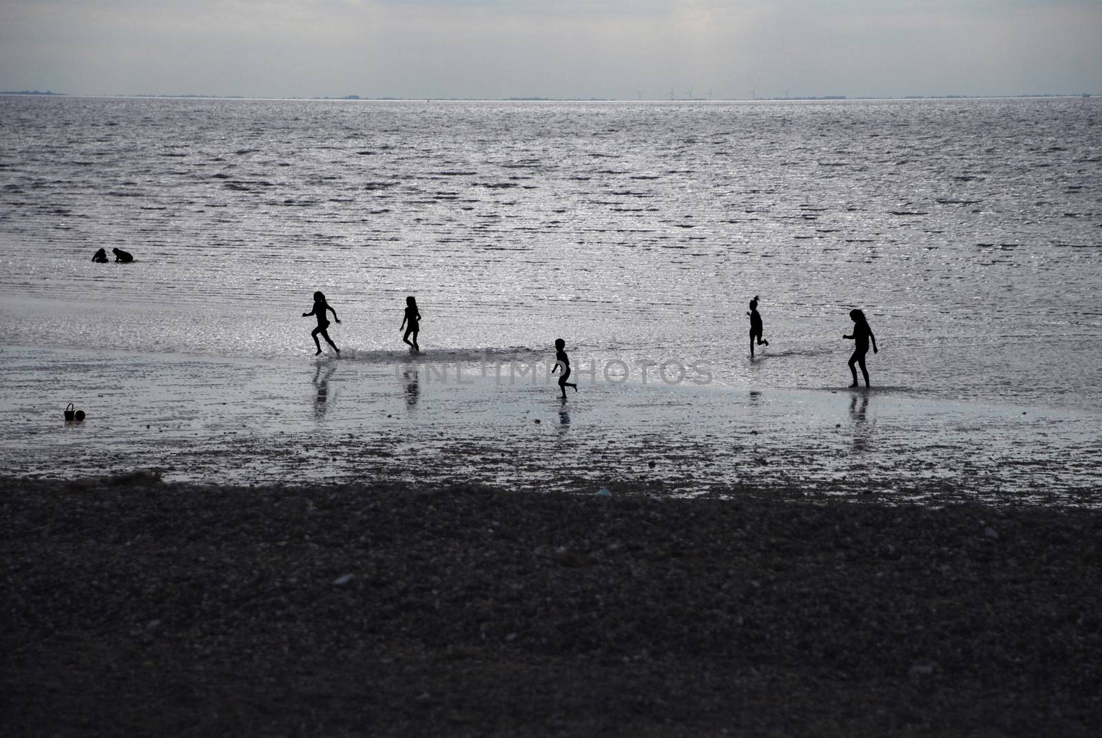 Silhouetted children - boys and girls - playing in the sea at sundown