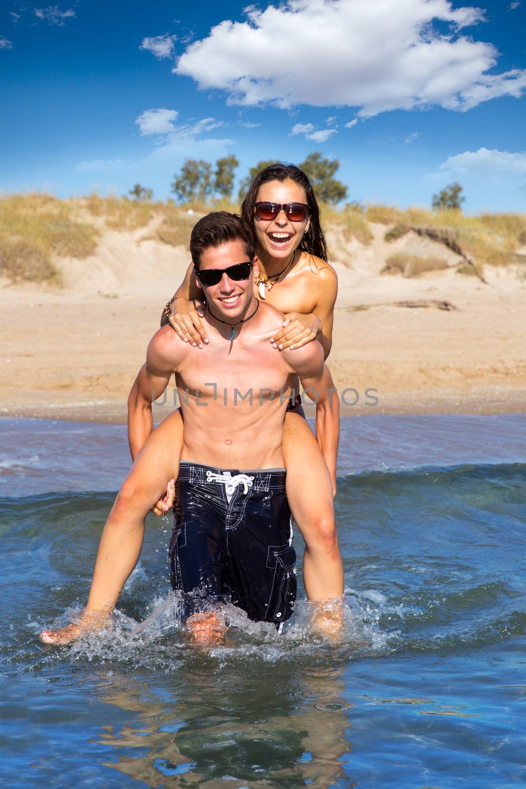 Teen couple running piggyback on summer beach splashing water