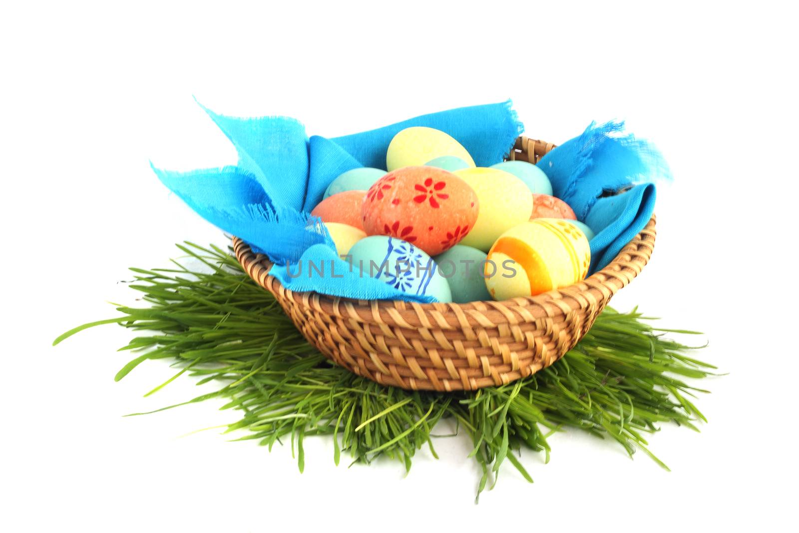 Basket of colored easter eggs in basket and grass on white background