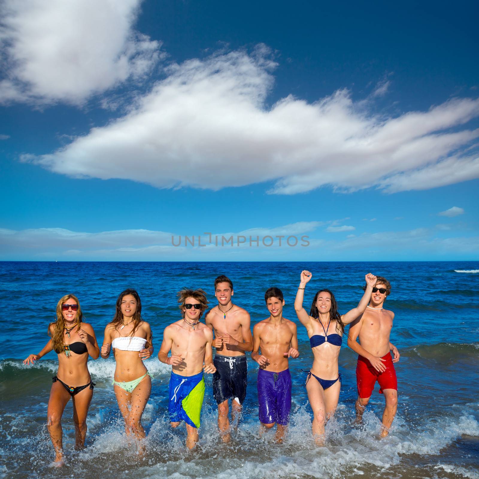 Teenagers group running happy splashing on the beach in summer vacations