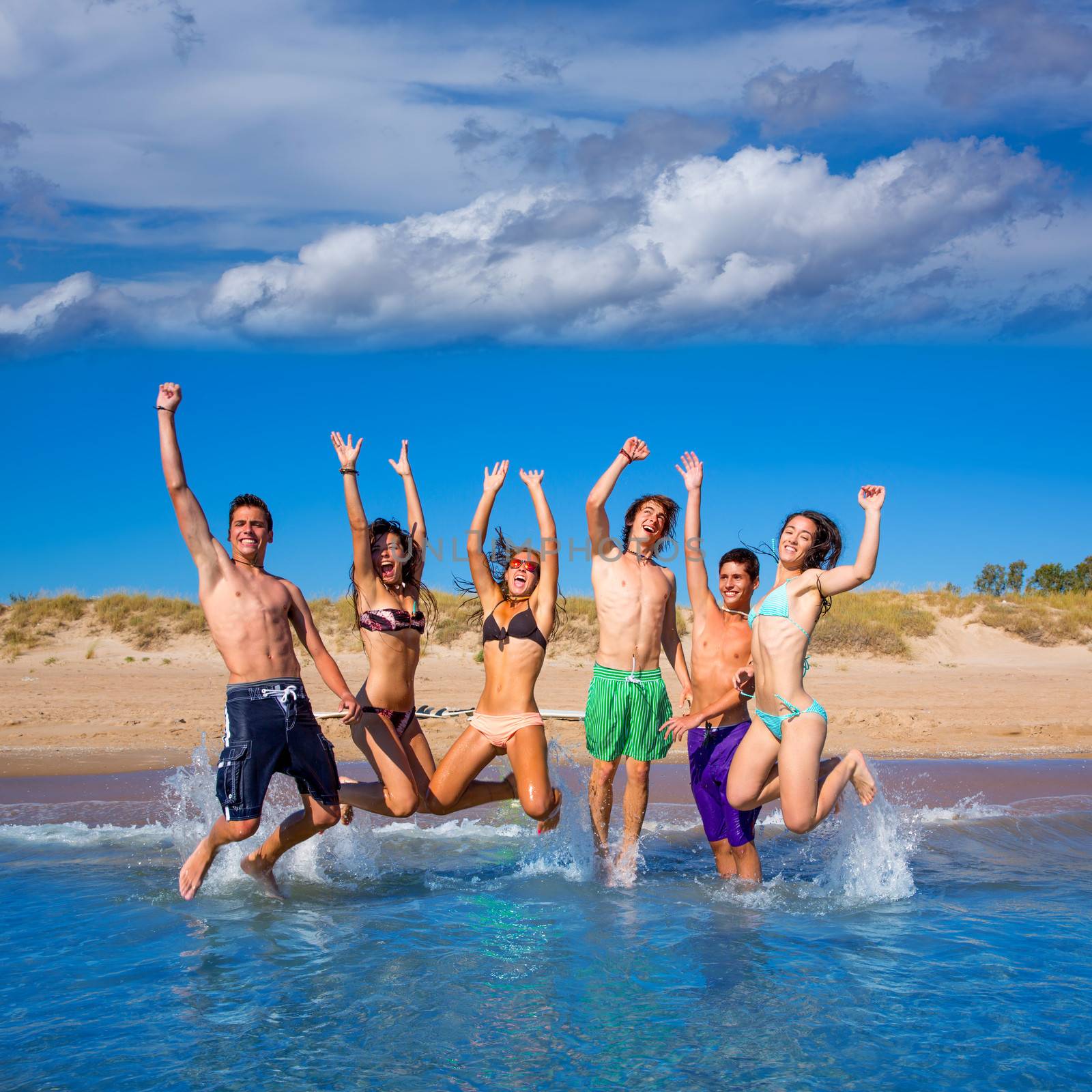 Happy excited teen boys and girls group jumping at the beach splashing water