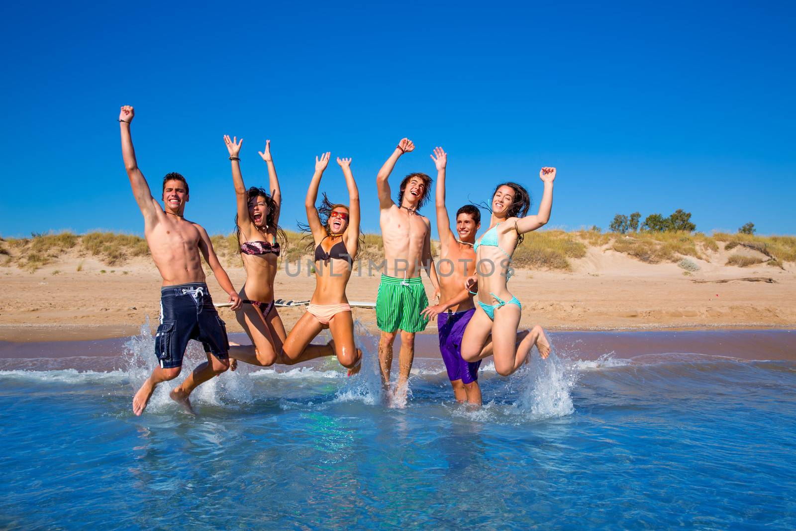 Happy excited teen boys and girls group jumping at the beach splashing water