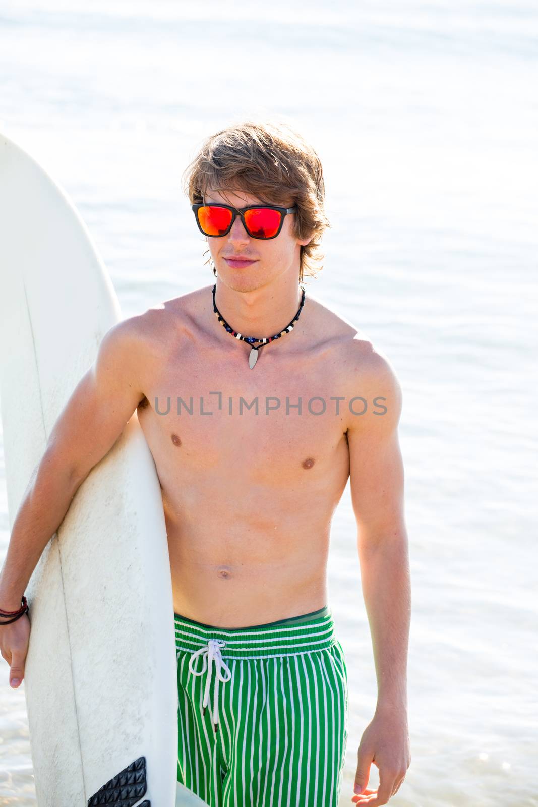 Boy teenager with surfboard on beach shore and orange sunglasses