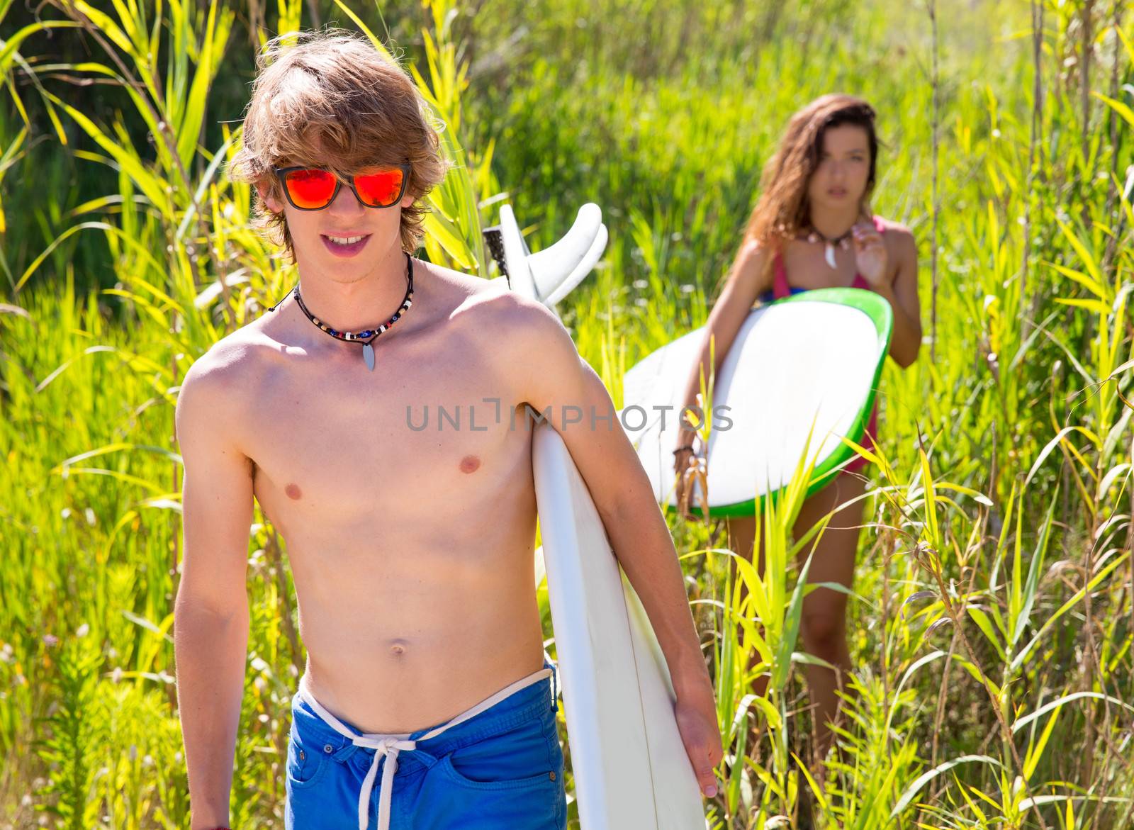 Surfer boy and girl walking in the green jungle with sunglasses