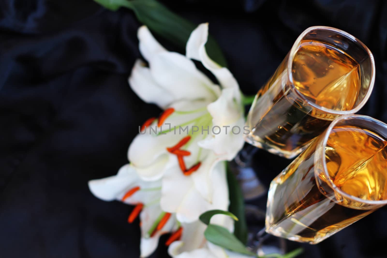 Glasses with wine and lily flower on black silk by destillat