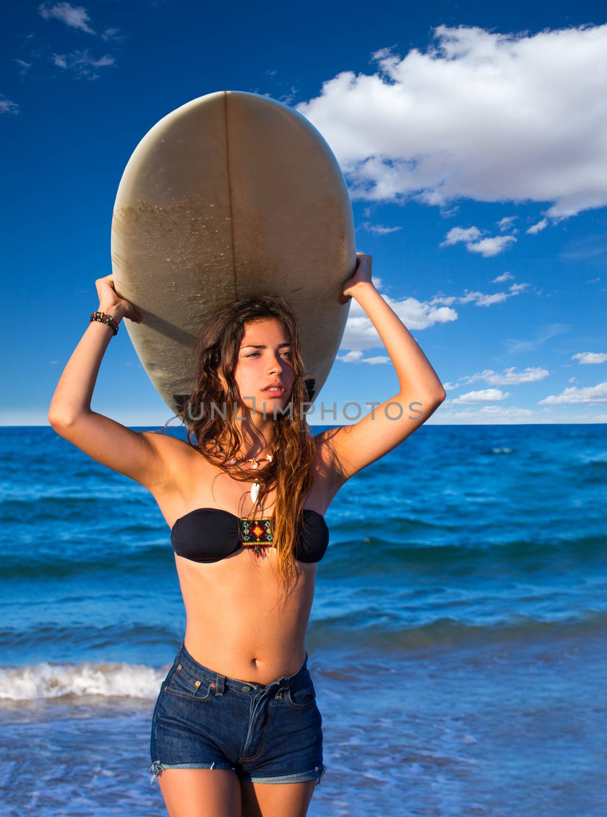 Brunette surfer teen girl holding surfboard in blue beach
