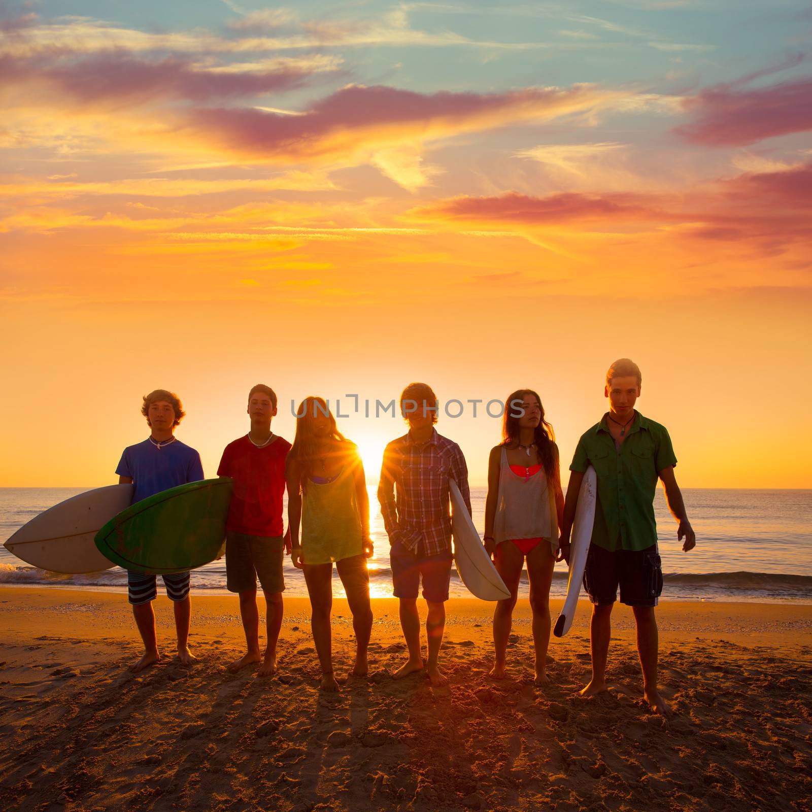 Surfers teen boys and girls group walking on beach at sunshine sunset backlight