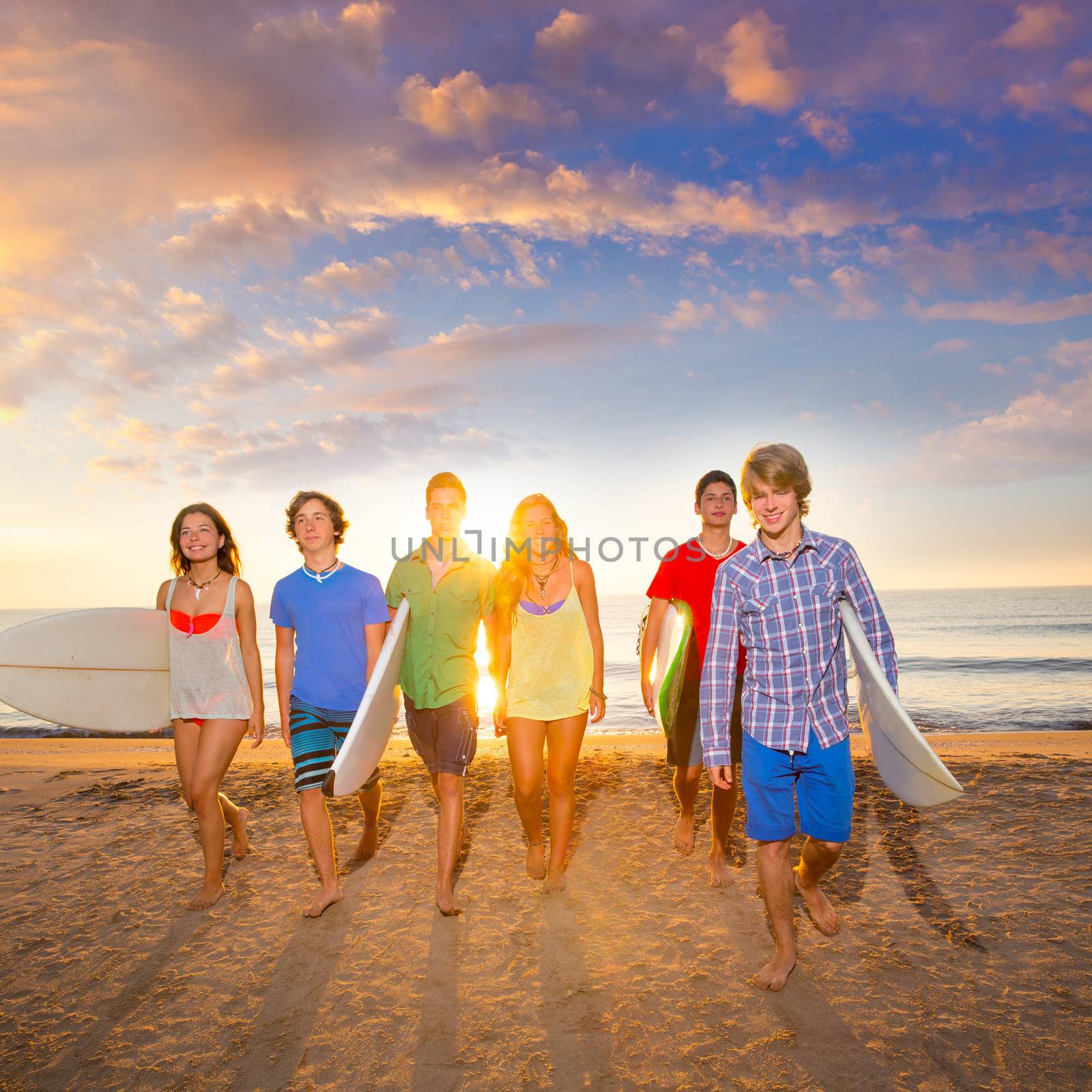 Surfers boys and girls group walking on beach by lunamarina