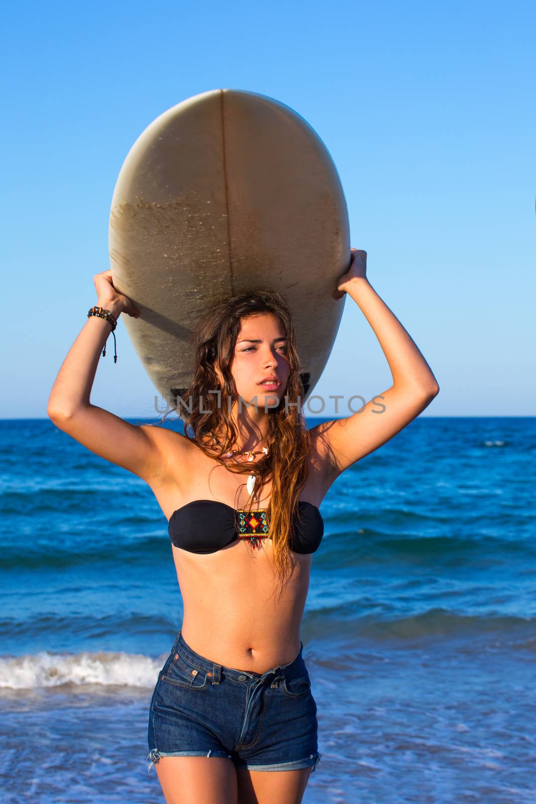 Brunette surfer teen girl holding surfboard in blue beach