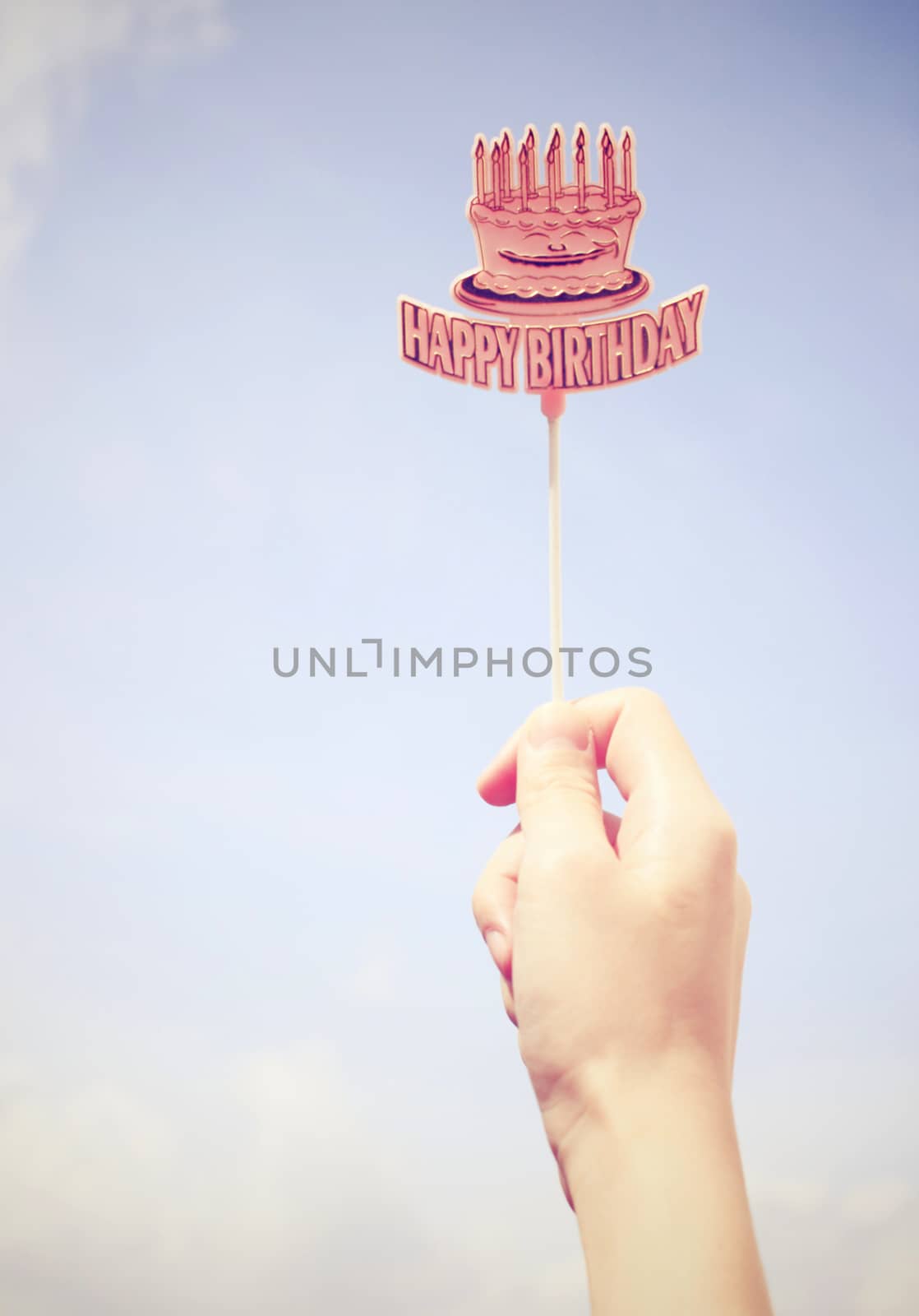 Hand holding happy birthday tag with blue sky, retro filter effect