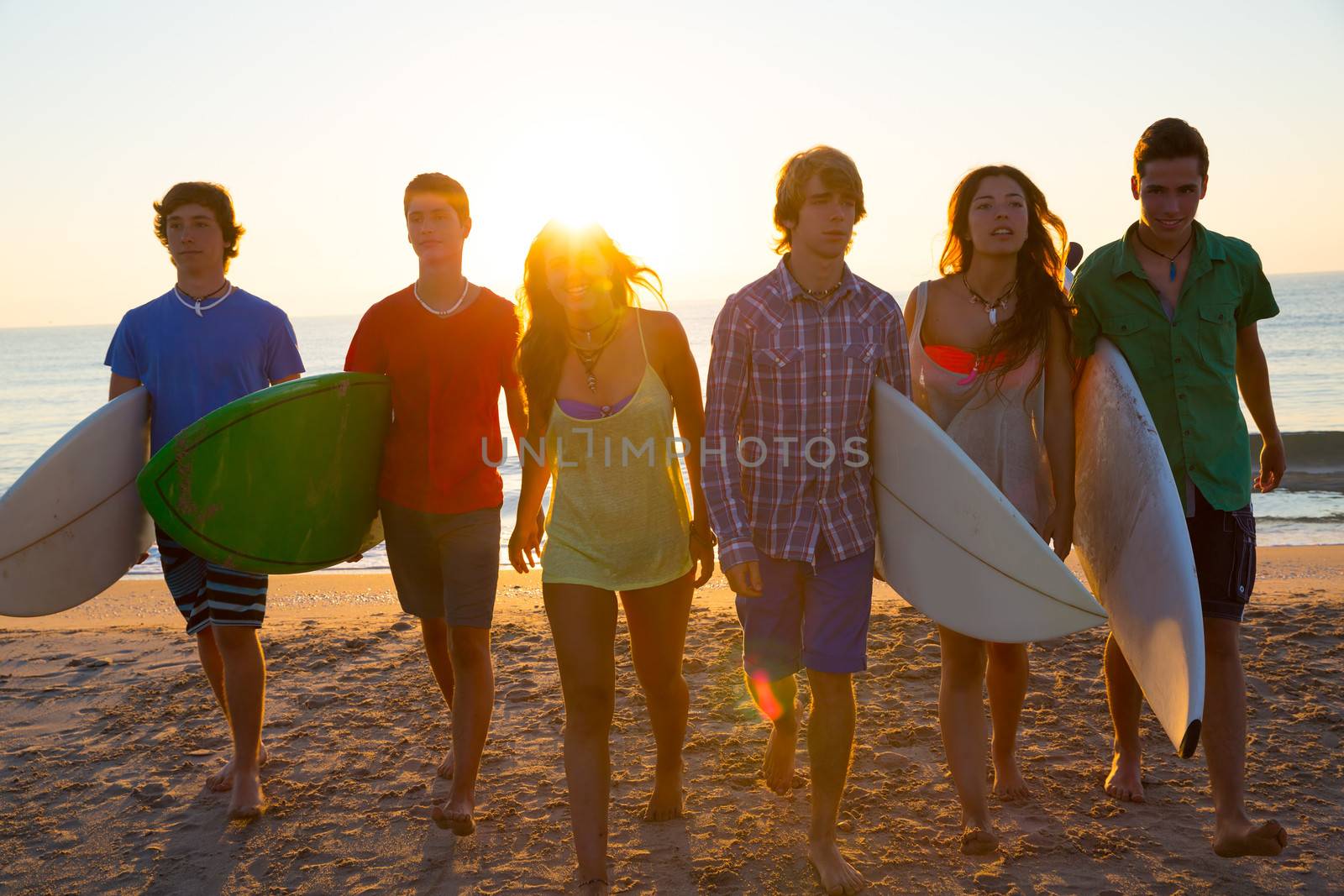 Surfers teen boys and girls group walking on beach at sunshine sunset backlight