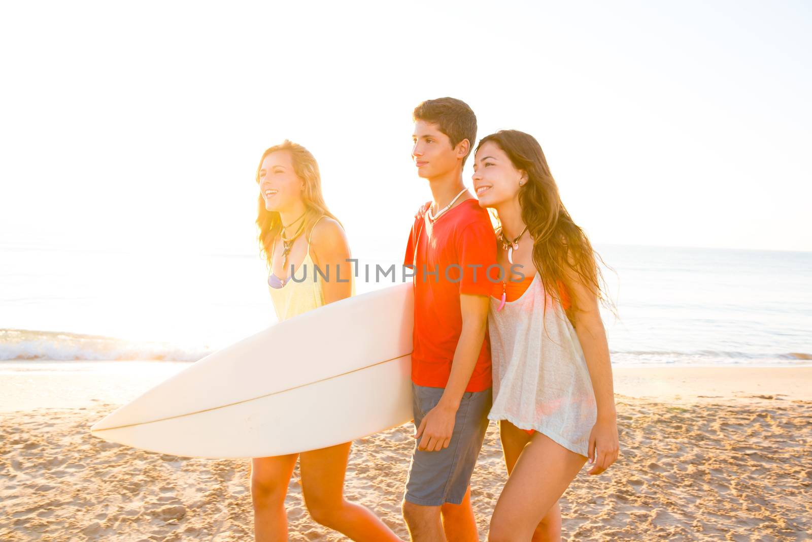 Surfer girls with teen boy walking on beach shore high key