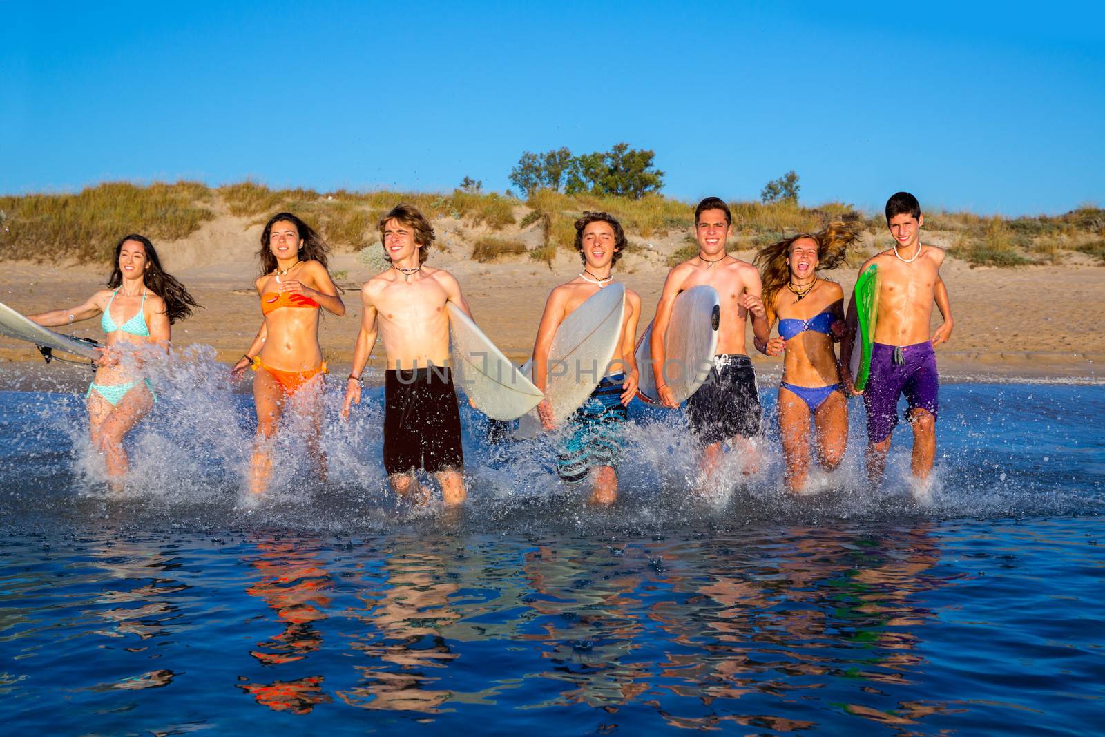 Teenager surfers group running beach splashing by lunamarina