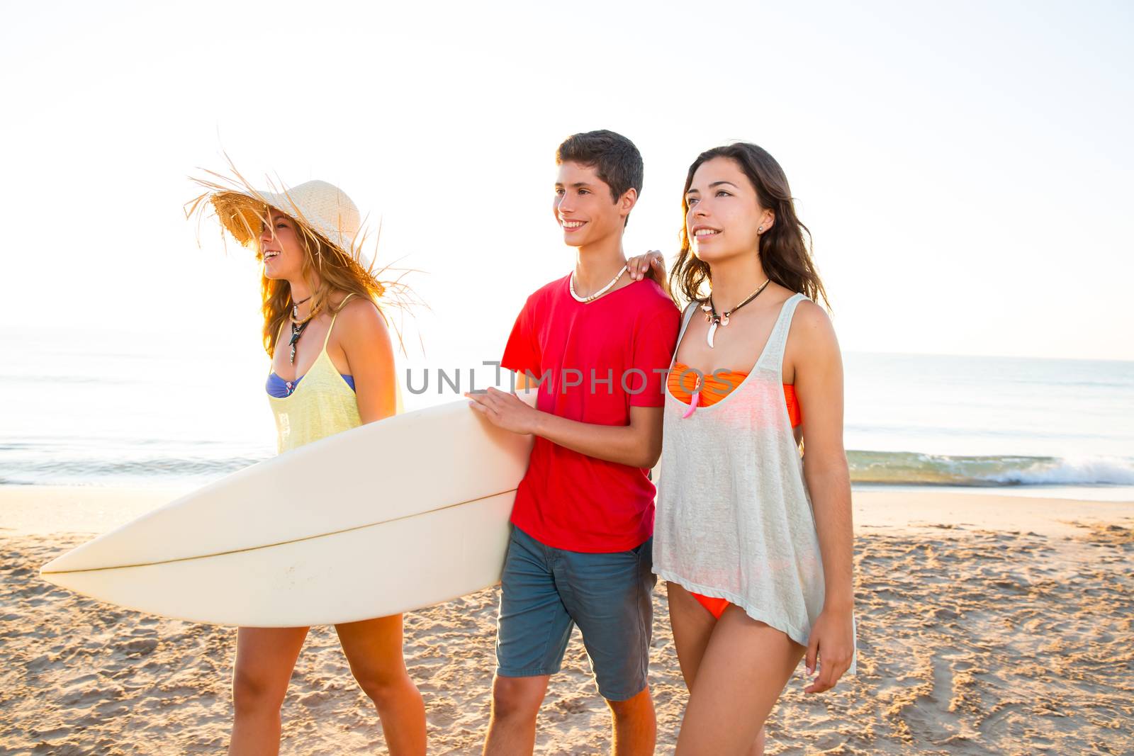 Surfer girls with teen boy walking on beach shore by lunamarina