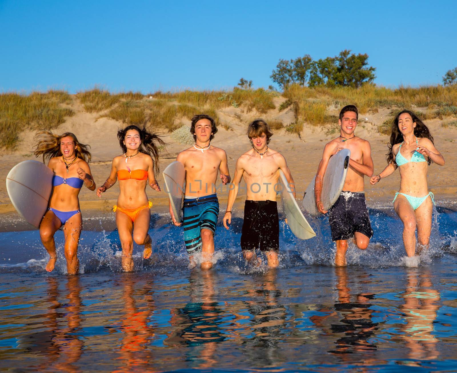 surfer teenagers boys and girls group running happy to the beach splashing water