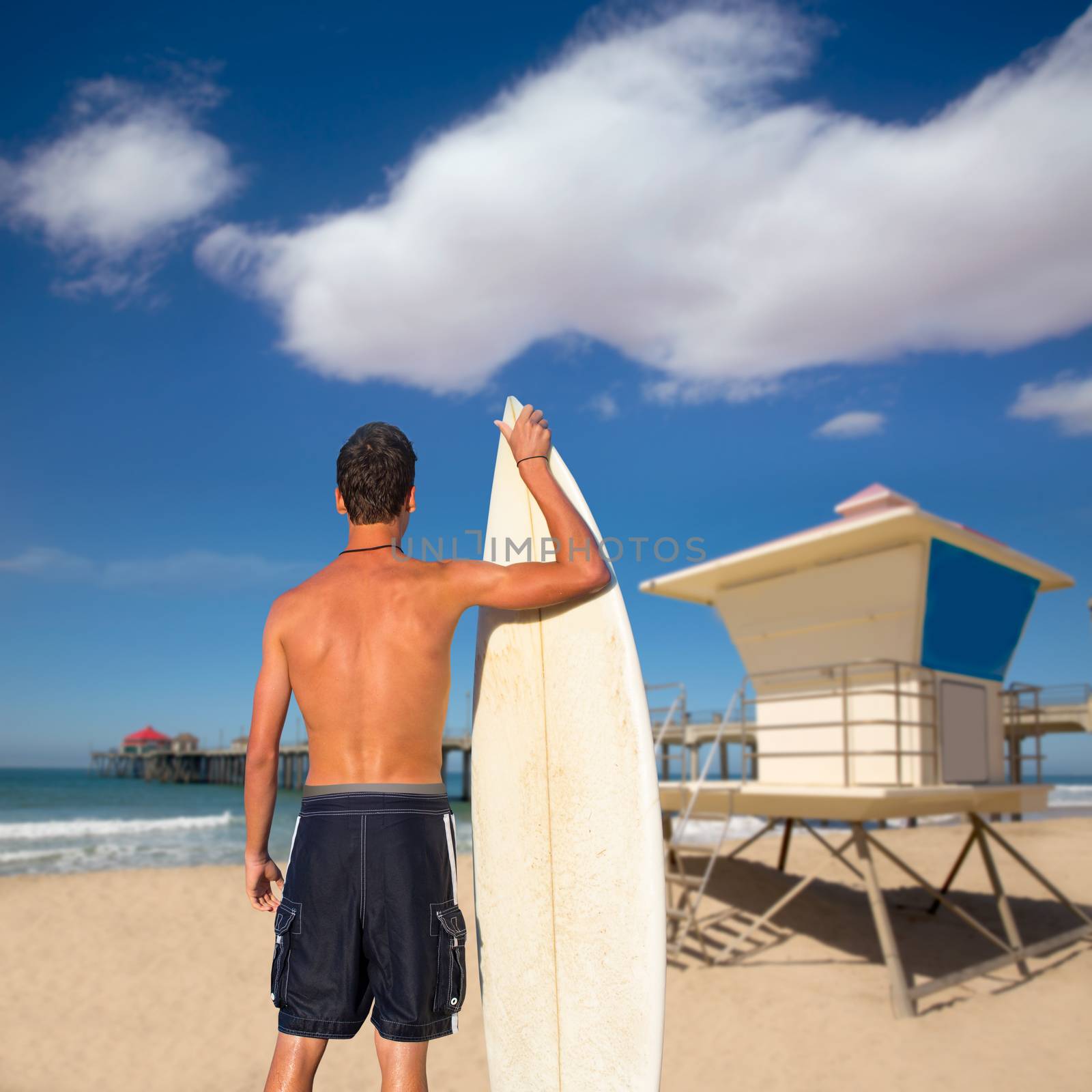 Boy surfer back rear view holding surfboard on Huntinton beach lifeguard house