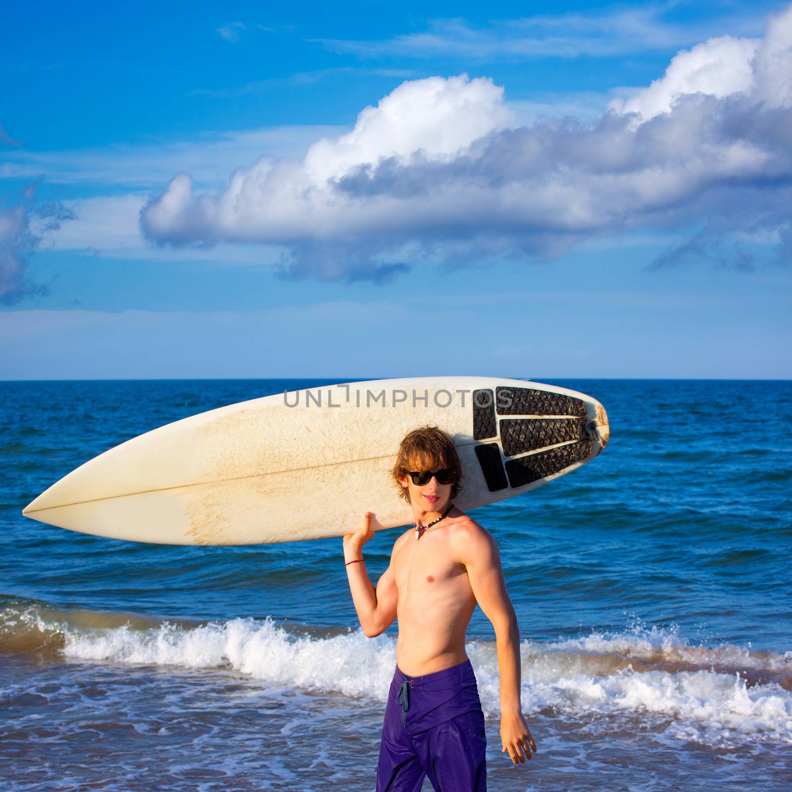 Boy teen surfer happy holing surfboard on the beach by lunamarina