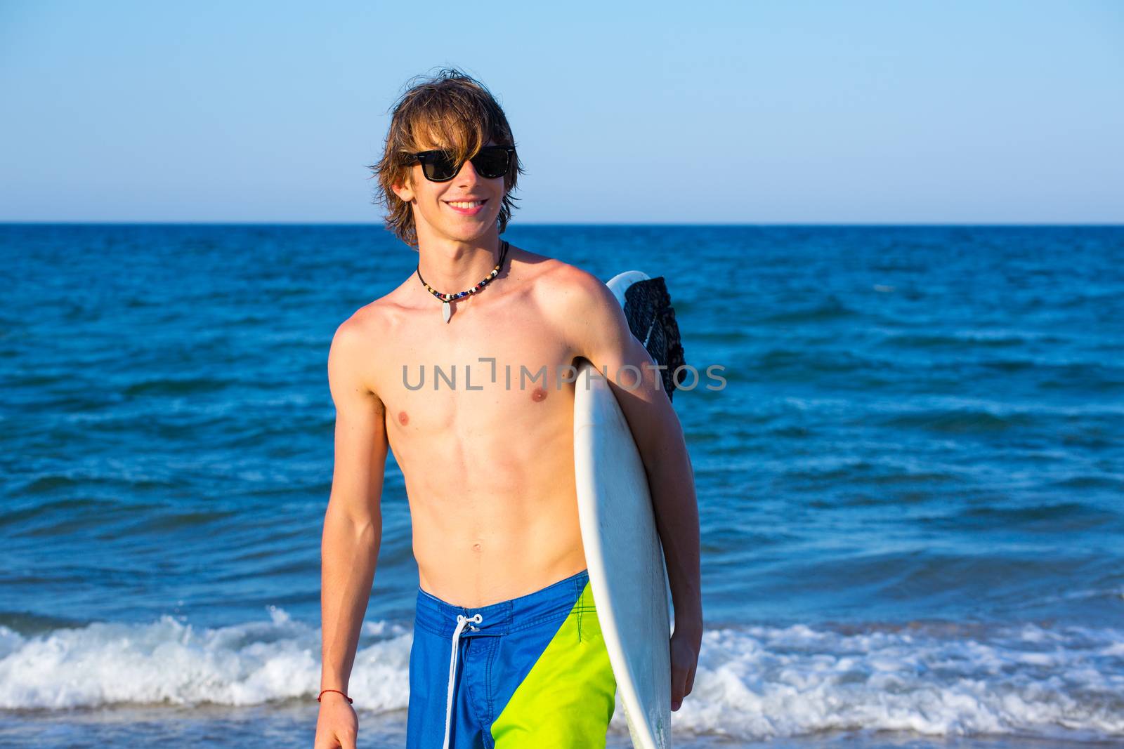 Boy teen surfer happy holing surfboard on the beach by lunamarina