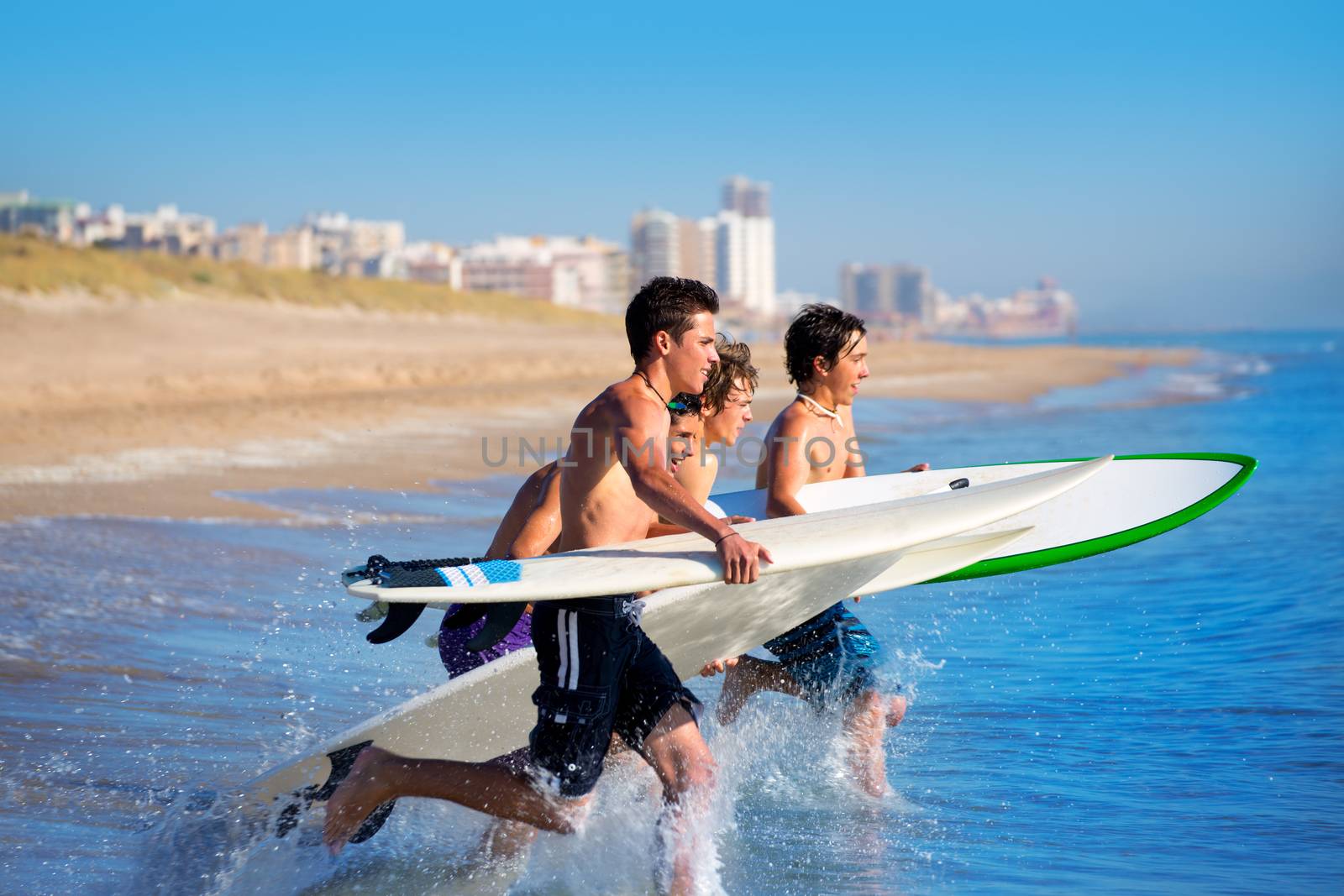 Teenager surfers surfing running jumping on surfboards at El Perello Cullera beach Spain