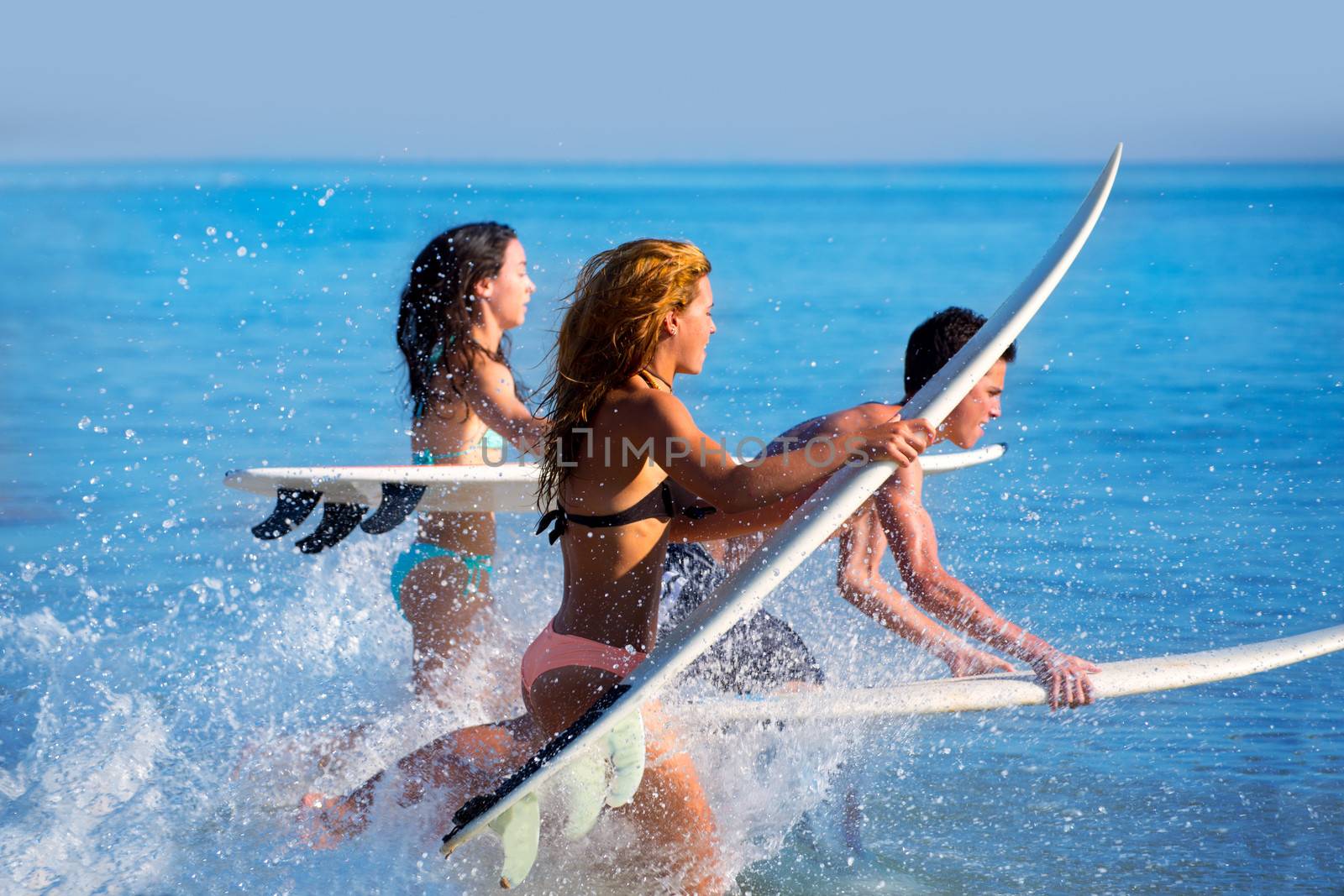 Boys and girls teen surfers running jumping on surfboards at the beach